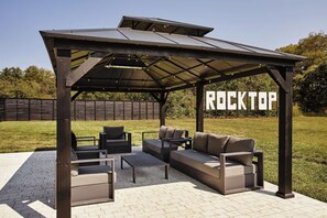A covered outdoor seating area with a pergola structure, labeled 'ROCKTOP,' featuring a sofa, chairs, and a small table.