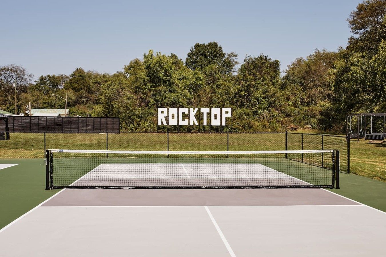 A tennis court with a net labeled 'ROCKTOP' and a surrounding fence.