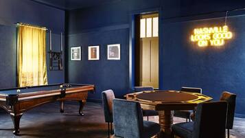 A room with a pool table, a billiards table, and a neon sign.