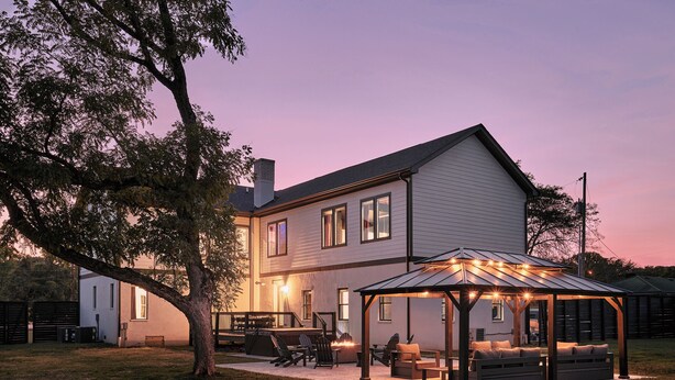 Een tweelaags huis met een overdekte patio, voorzien van buitenmeubels en een vuurkorf.