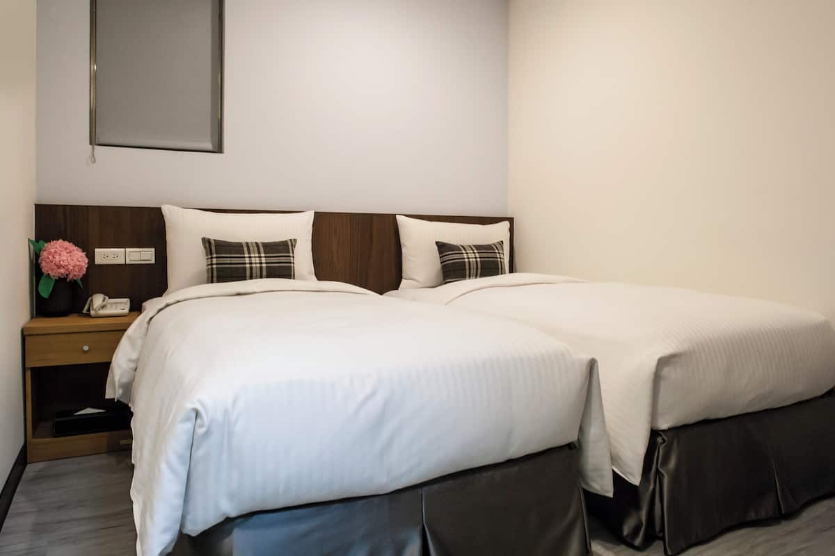 A double bed with white linens, a wooden headboard, and a bedside table with a phone and a vase of flowers.