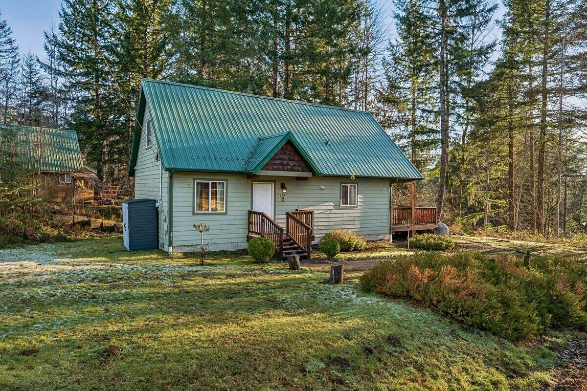 A single-story cabin with a green metal roof, a front porch, and a small deck.