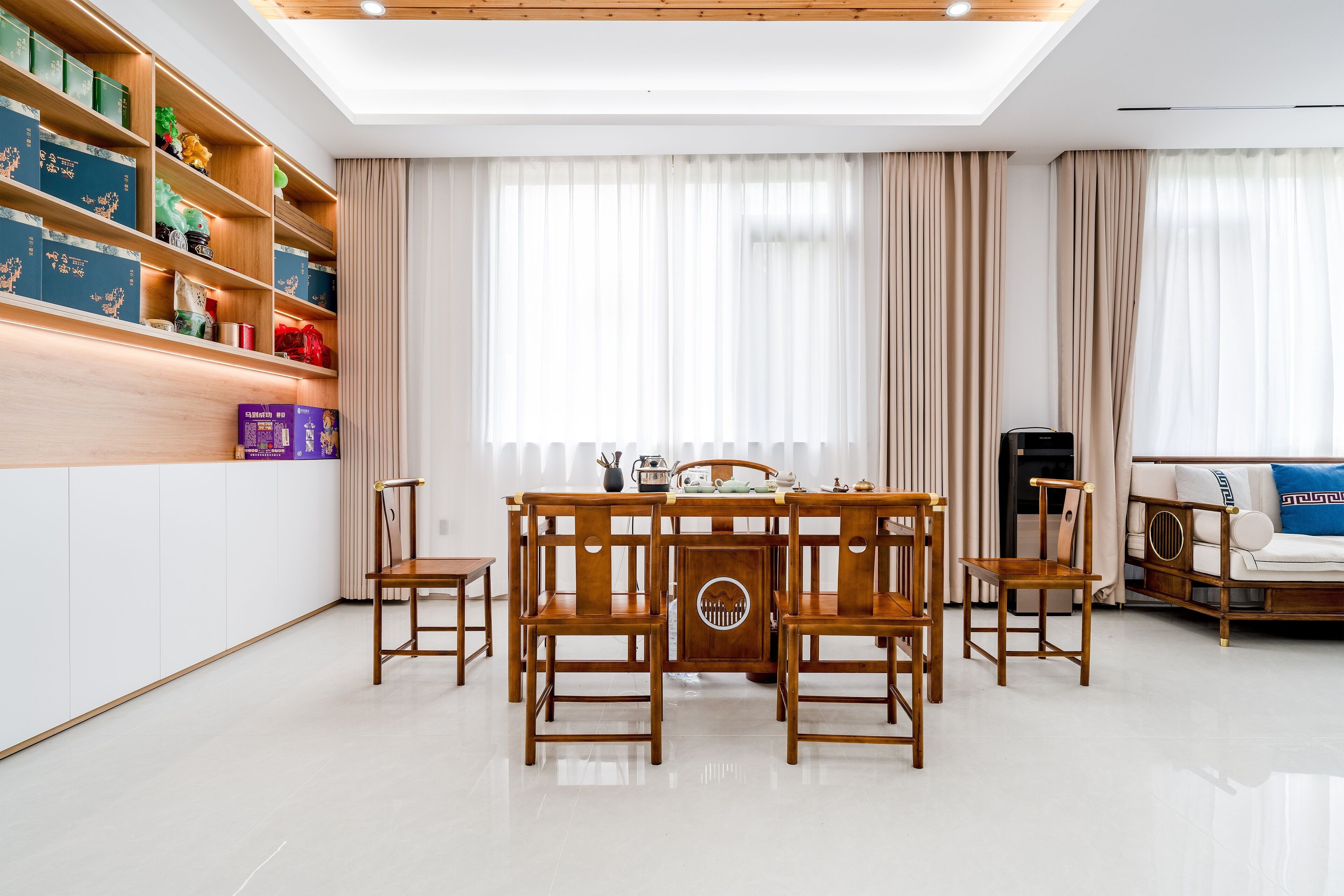 A dining area with a wooden table and chairs, a bookshelf with various items, and a sofa with a decorative pillow.