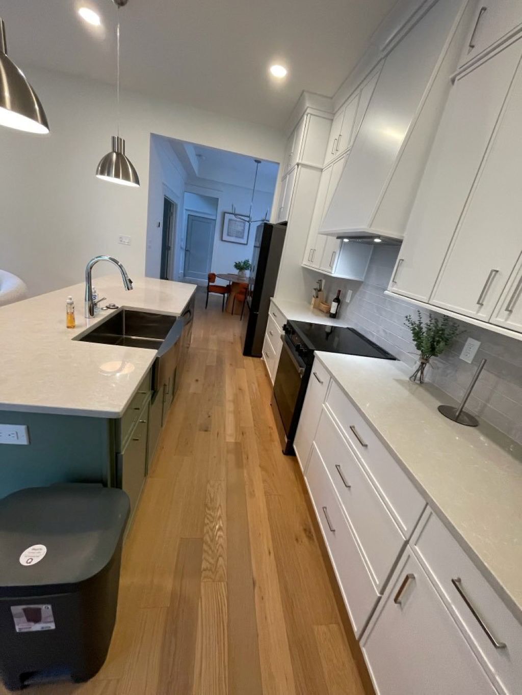 A modern kitchen with white cabinets, a central island, and a dining area in the background.