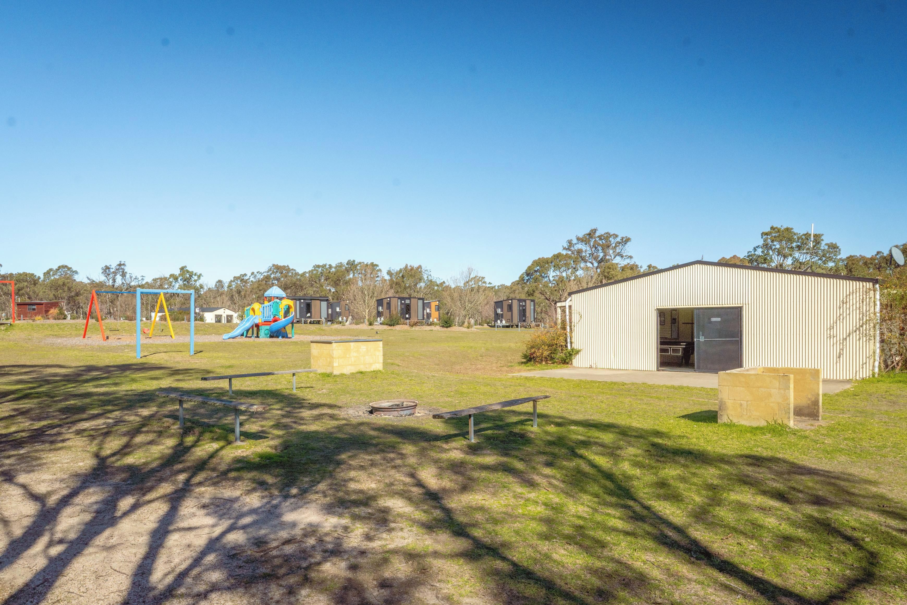 A playground with slides and swings, a building with a door, and a grassy area with benches.