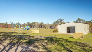 A playground with slides and swings, a building with a door, and a grassy area with benches.