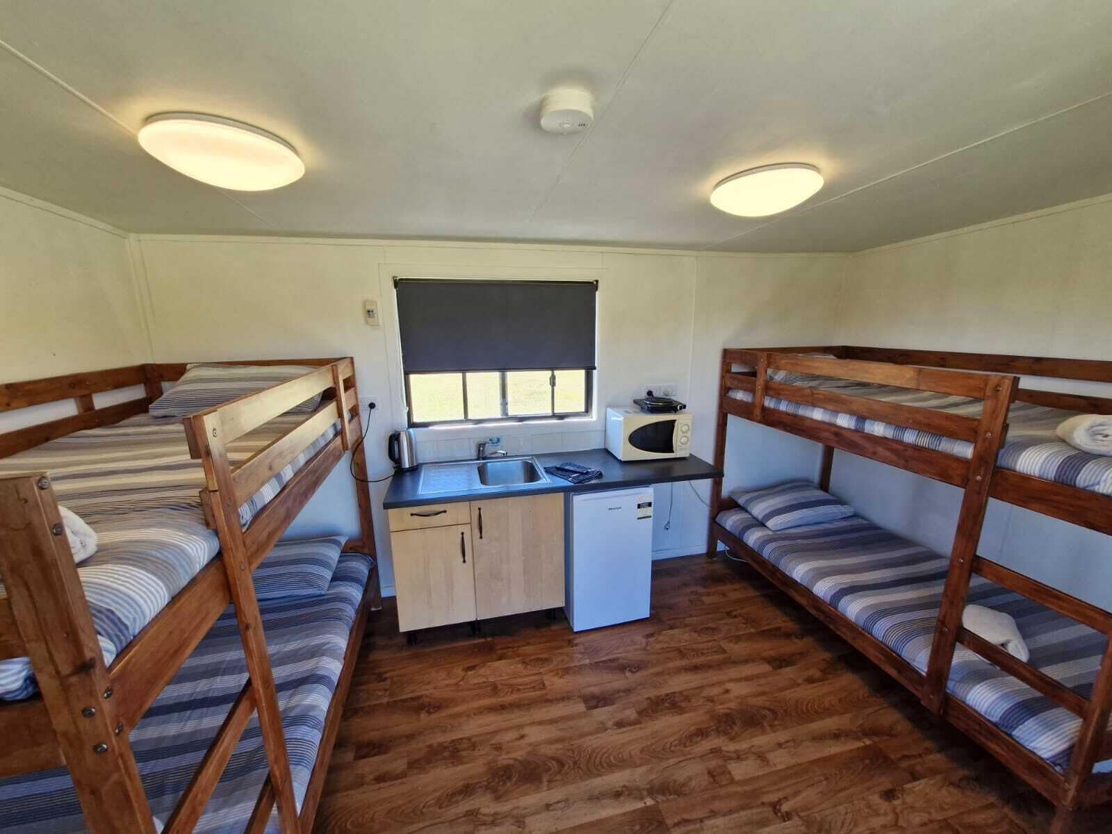 A compact room with bunk beds, a small kitchenette, and a window with blinds.