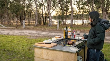 An outdoor barbecue setup with a grill, food items, and beverages on a portable table.