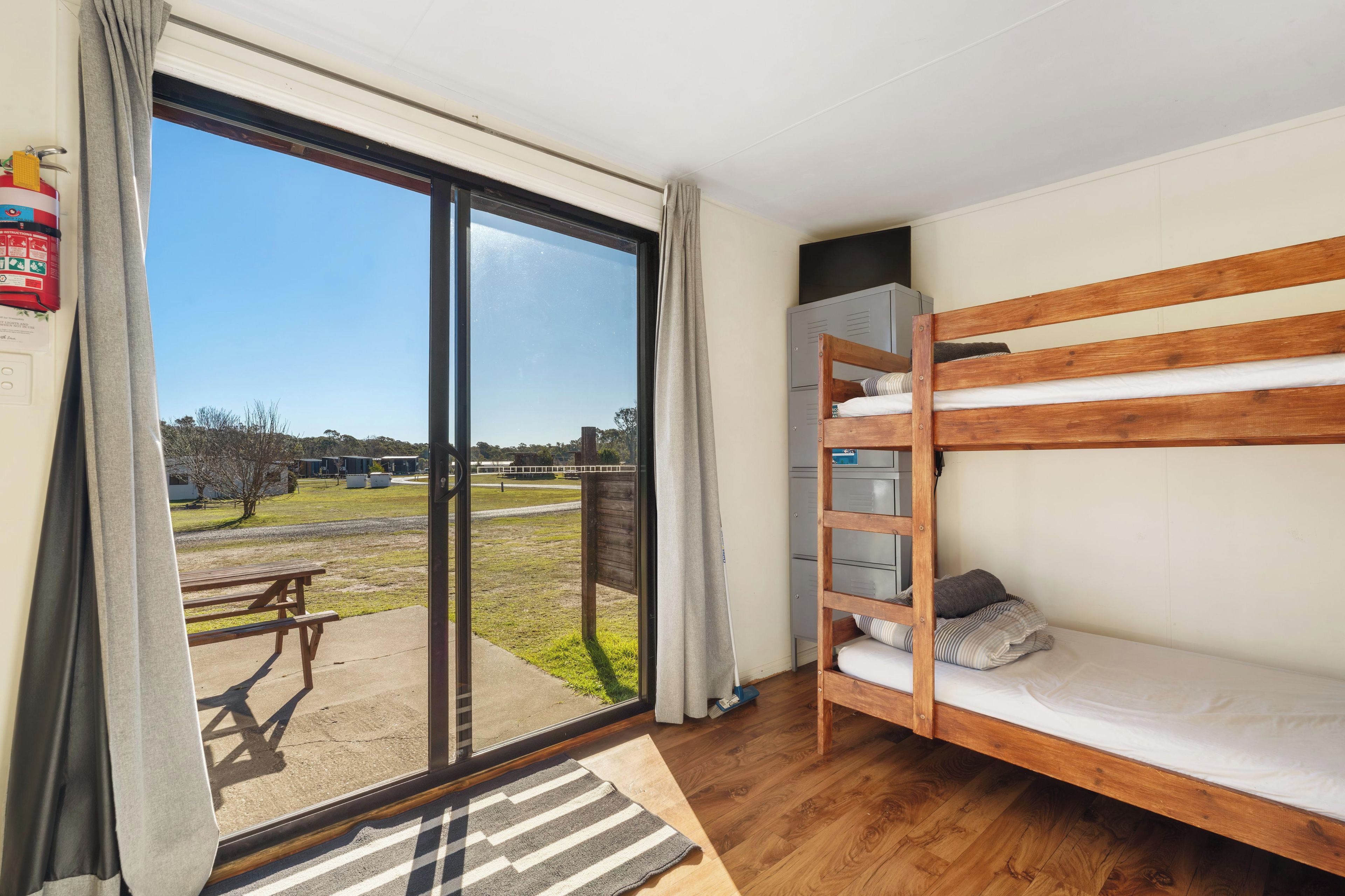 A room with a bunk bed, a sliding glass door leading to an outdoor area, and a small table.