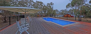 A wooden deck with a pool, lounge chairs, and umbrellas.