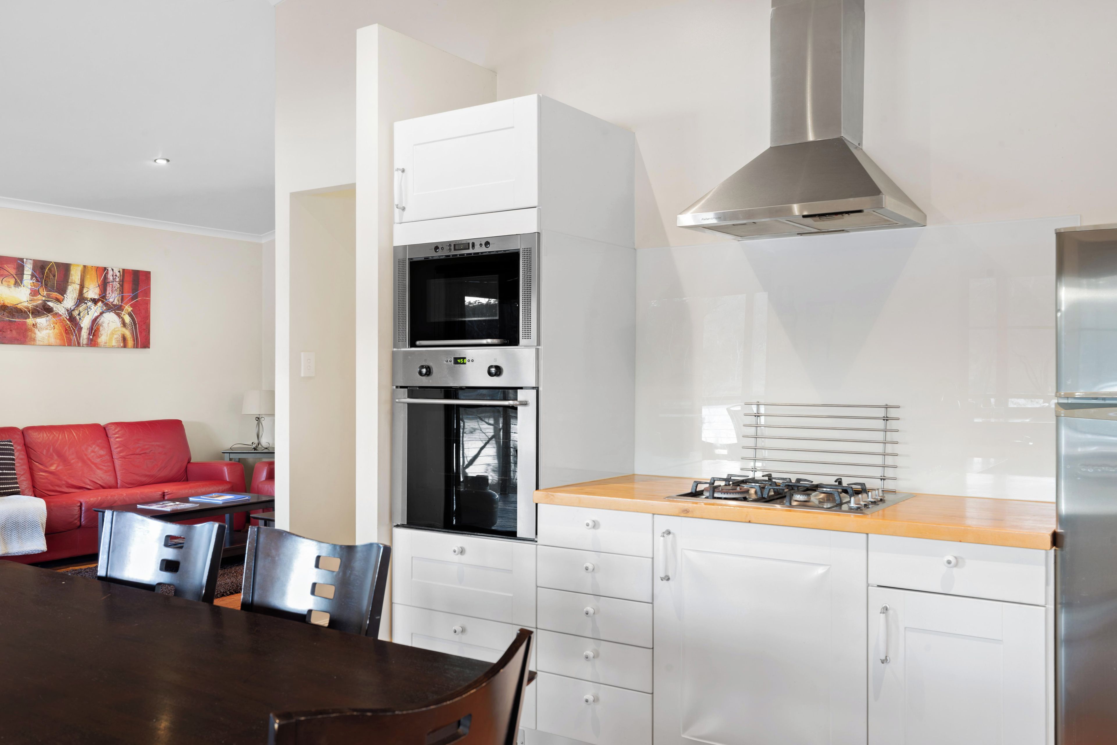 A modern kitchen with white cabinetry, a built-in oven, a gas stove, and a stainless steel range hood.