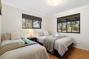 A bedroom with two beds, a nightstand, a lamp, and windows with blinds. - Tiny Away Escape at Granite Belt (Stanthorpe)