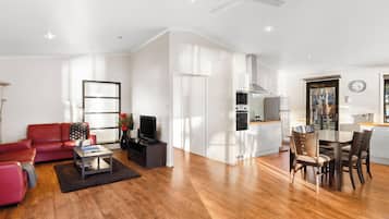 A modern living space with a red sofa, a coffee table, a TV, and a dining area with chairs and a table.
