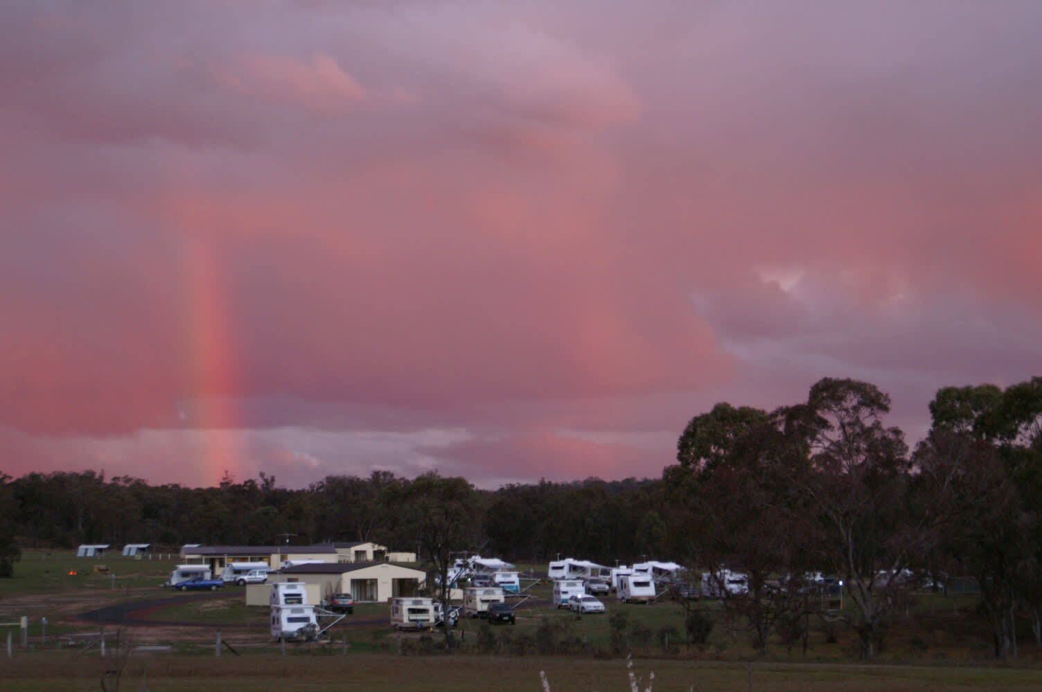 Un camping con vehículos recreativos y casas móviles, rodeado de árboles y un cielo nublado.