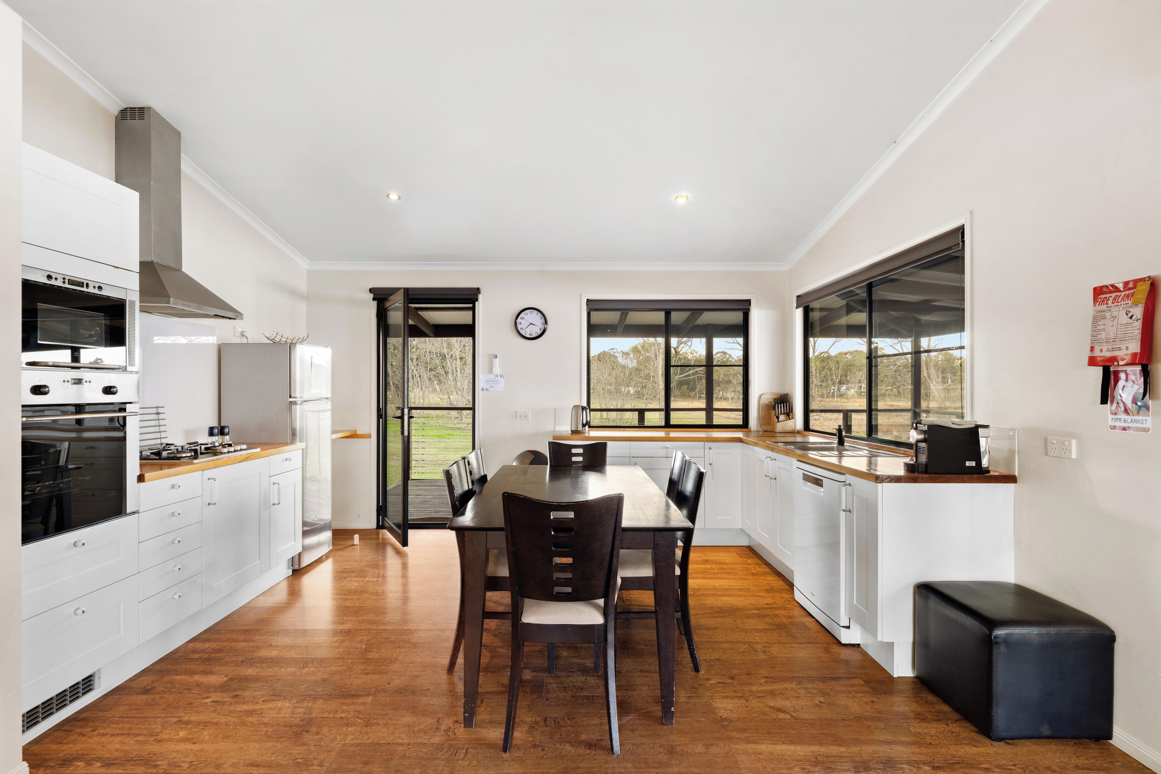 A modern kitchen with white cabinetry, a built-in oven, and a dining area with a wooden table and chairs.