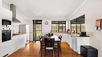 A modern kitchen with white cabinetry, a built-in oven, and a dining area with a wooden table and chairs.