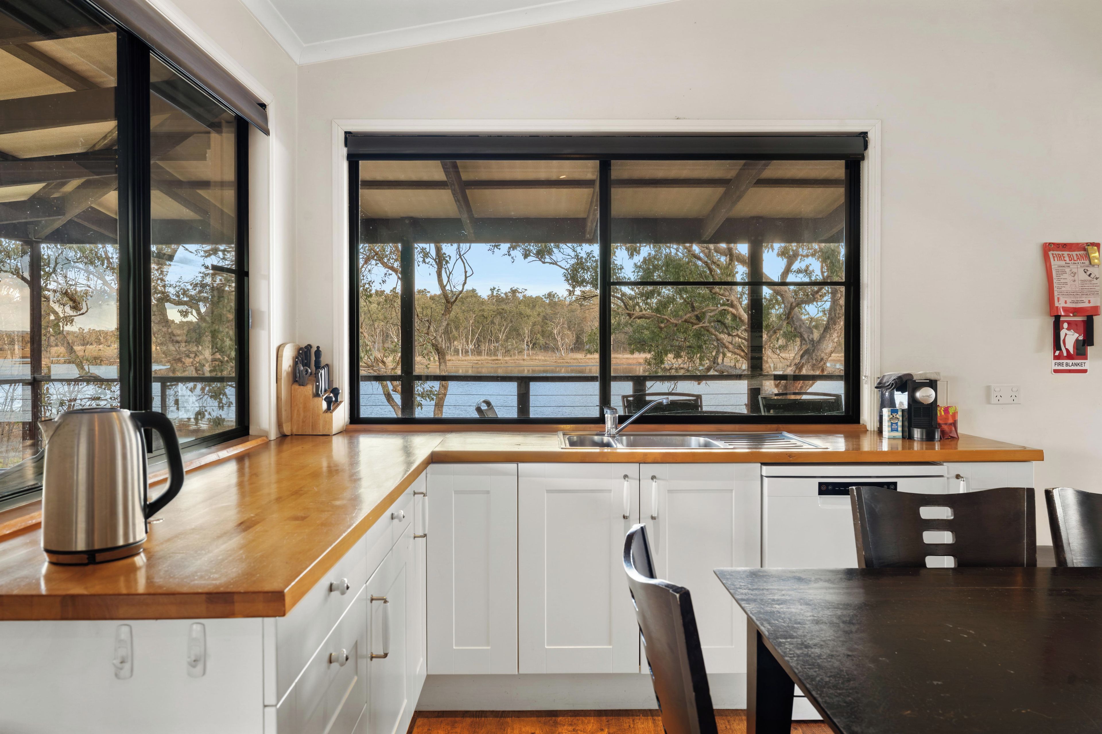 A modern kitchen with a large window, white cabinets, a wooden countertop, and a view of a lake.