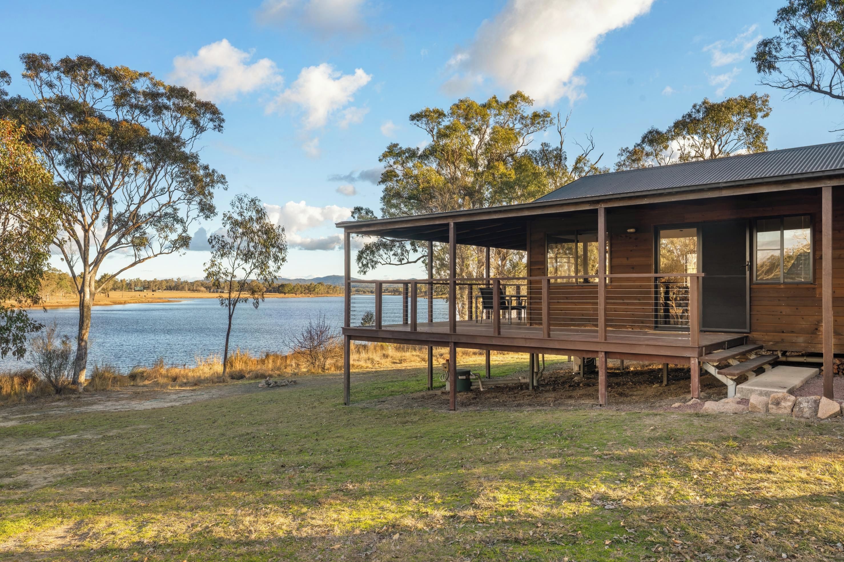 A wooden cabin with a deck overlooking a lake, surrounded by trees.