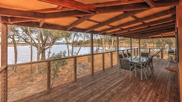 A covered outdoor deck with a table and chairs, overlooking a body of water and trees.
