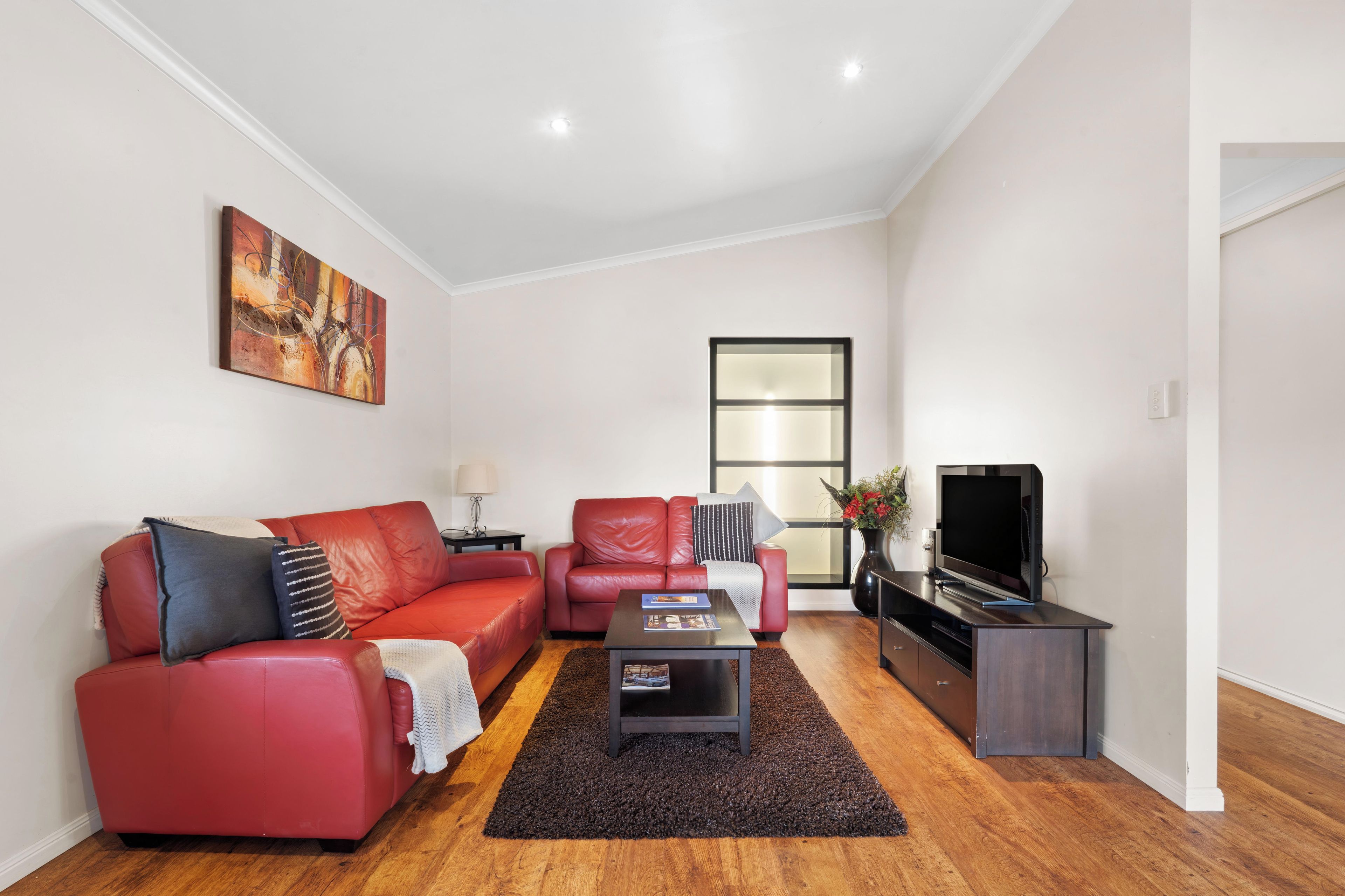 Ein modernes Wohnzimmer mit einem roten Sofa, einem Couchtisch, einem Fernseher und einem Gemälde an der Wand.
