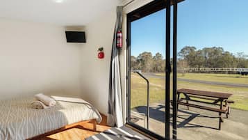 A room with a bed, a fire extinguisher, and a view of a park through a glass door.