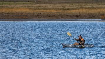 A person kayaking on a body of water with a grassy field in the background.