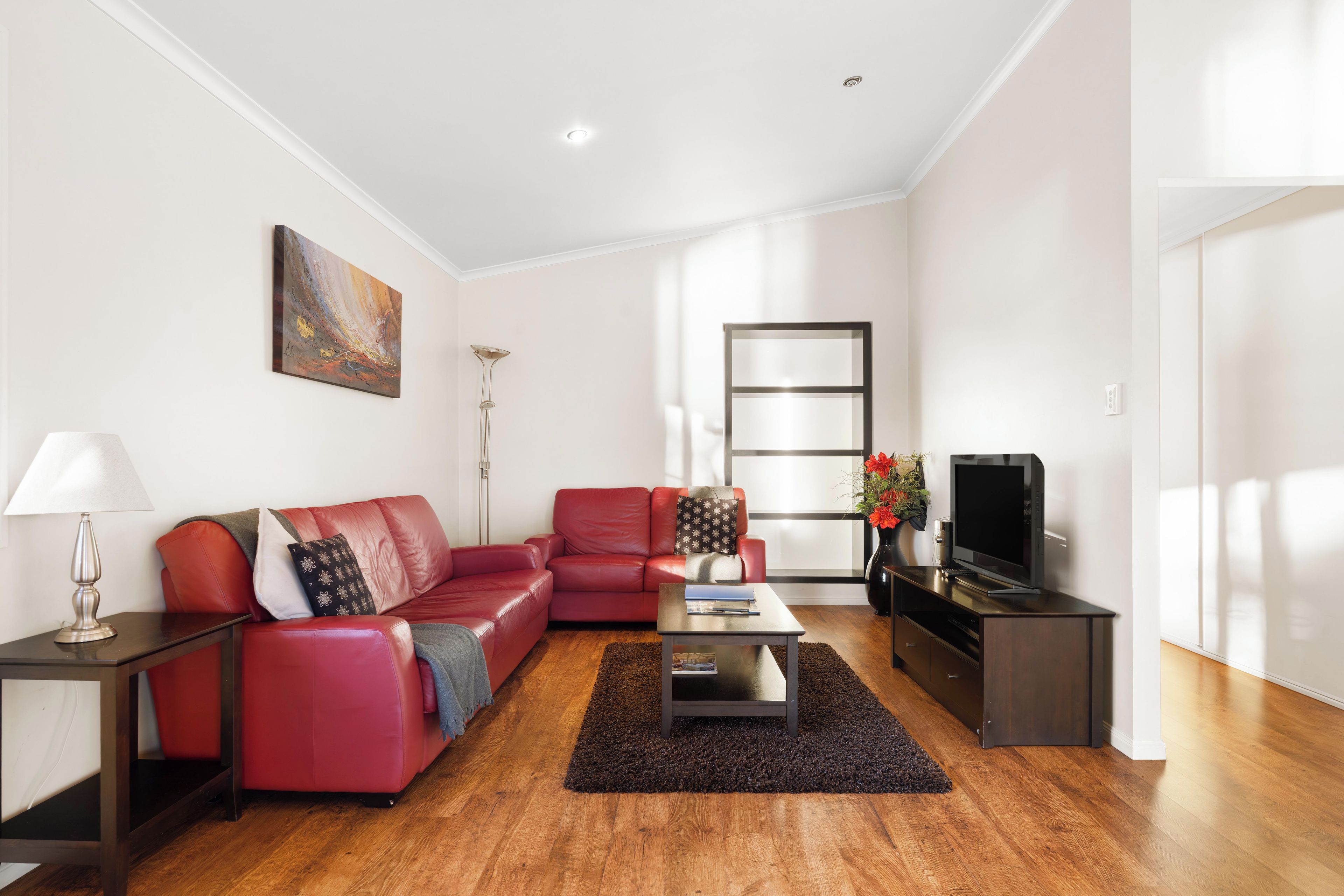 Uma sala de estar moderna com um sofá vermelho, uma mesa de centro, uma televisão e um quadro na parede.