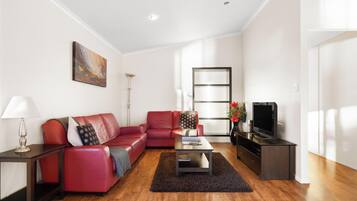 Uma sala de estar moderna com um sofá vermelho, uma mesa de centro, uma televisão e um quadro na parede.