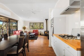 A modern kitchen with a central island, a dining area with a table and chairs, and a living area with a sofa and a fireplace. - Tiny Away Escape at Granite Belt (Stanthorpe)