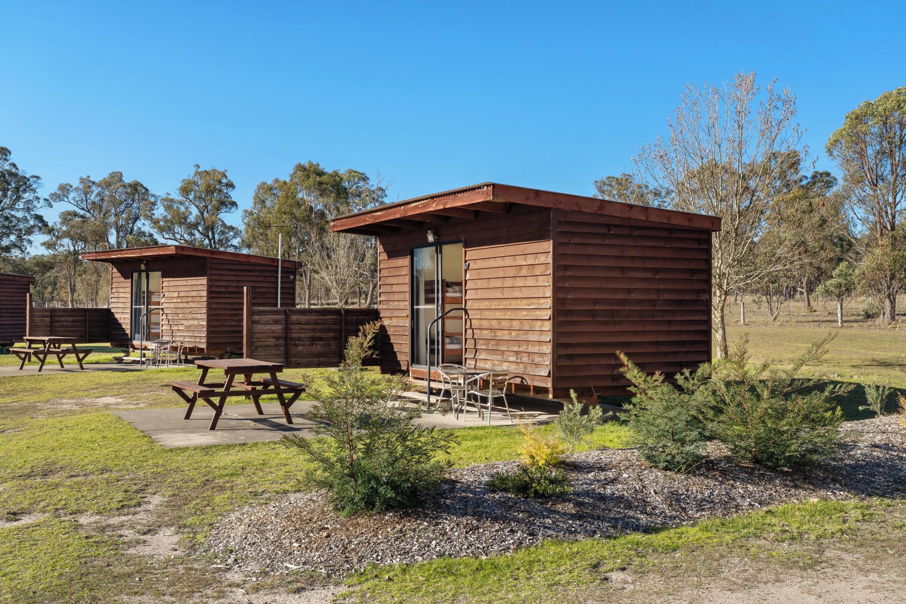 Un camping con cabañas de madera, mesas de picnic y cielo despejado.