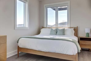 Une chambre à coucher avec un lit, deux fenêtres, une table de chevet et une commode.