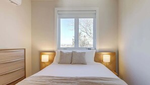 A hotel room with a bed, bedside lamps, a window, and a wooden dresser. - Pet-Friendly in Belmont near UVA & Downtown - #311 (Charlottesville)