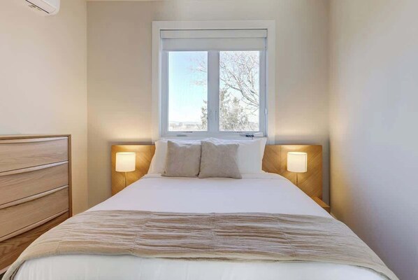 Une chambre d’hôtel avec un lit, des lampes de chevet, une fenêtre et une commode en bois.