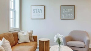 A living room with a brown leather sofa, a round wooden side table, a grey armchair, and two framed motivational quotes on the wall. - Pet-Friendly in Belmont near UVA & Downtown - #311 (Charlottesville)