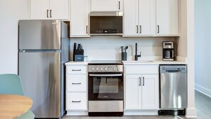 A modern kitchen with stainless steel appliances, white cabinetry, and a dining area with a table and chairs. - Pet-Friendly in Belmont near UVA & Downtown - #311 (Charlottesville)