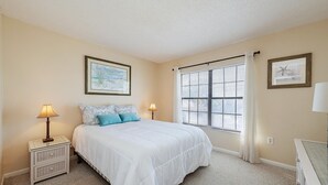 A bedroom with a large bed, two bedside tables with lamps, a window with blinds, and two framed pictures on the walls. - San marco villas 2-bedroom newly updated condo in lovely Marco Island  (Marco Island)