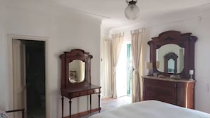 Een slaapkamer met een bed, twee houten kledingkasten, een spiegel en een deur naar een andere kamer.