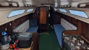 A narrow interior with two blue cushioned seating areas, a central aisle, and a green carpet.