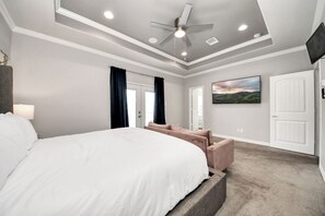 Ein Schlafzimmer mit einem großen Bett, einem Deckenventilator, Einbauleuchten, einem Gemälde und einer Tür.
