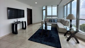 A modern living room with a large TV, a glass coffee table, a sofa, and a view of the ocean. - Almendra I Spacious 1 Bedroom With Balcony (Panama City)