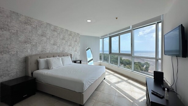 A modern bedroom with a large bed, a TV, and a view of the ocean. - Almendra I Spacious 1 Bedroom With Balcony (Panama City)