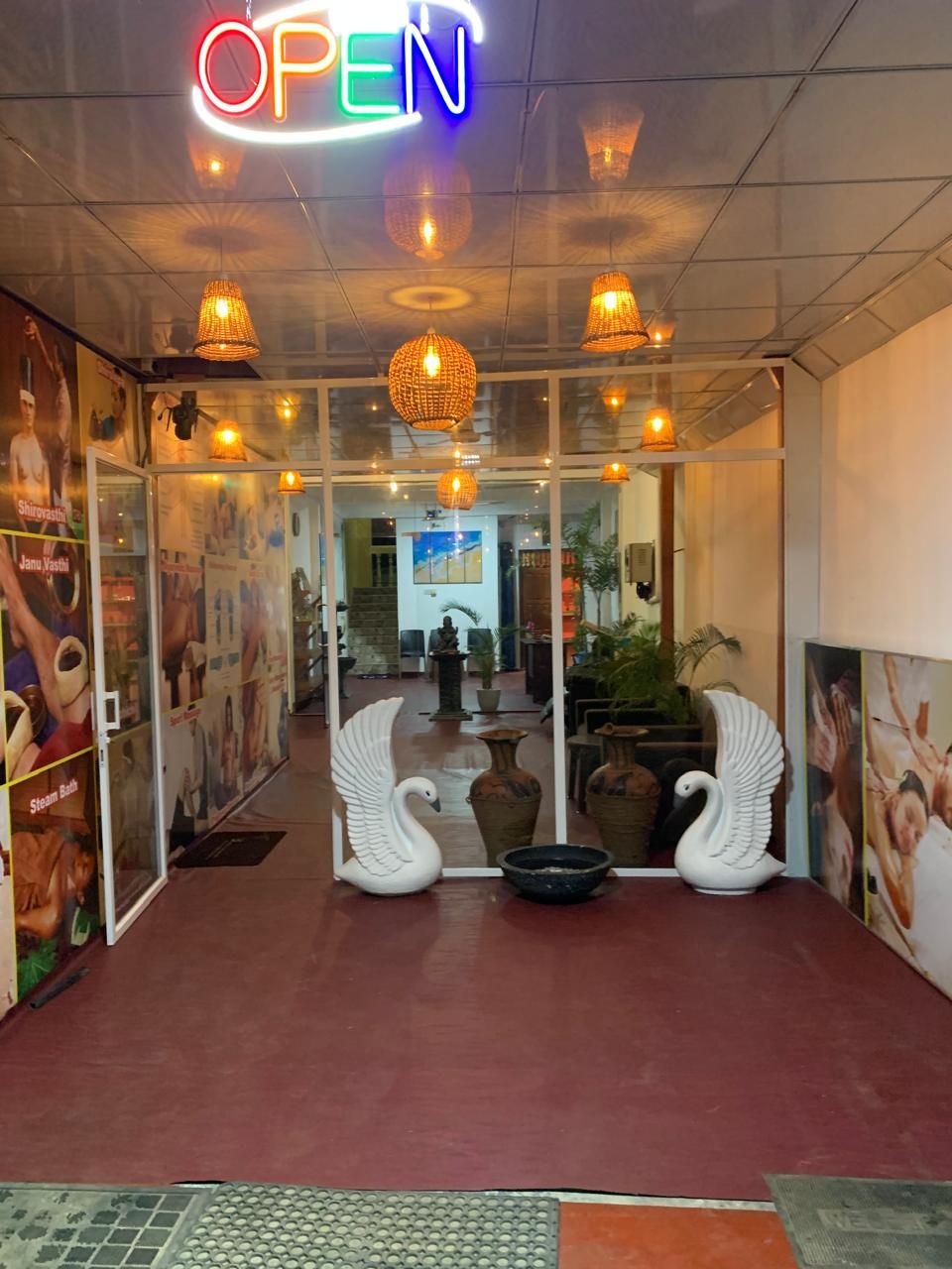 Entrada de hotel con un letrero de neón que dice 'OPEN', esculturas decorativas de cisnes y lámparas de mimbre.