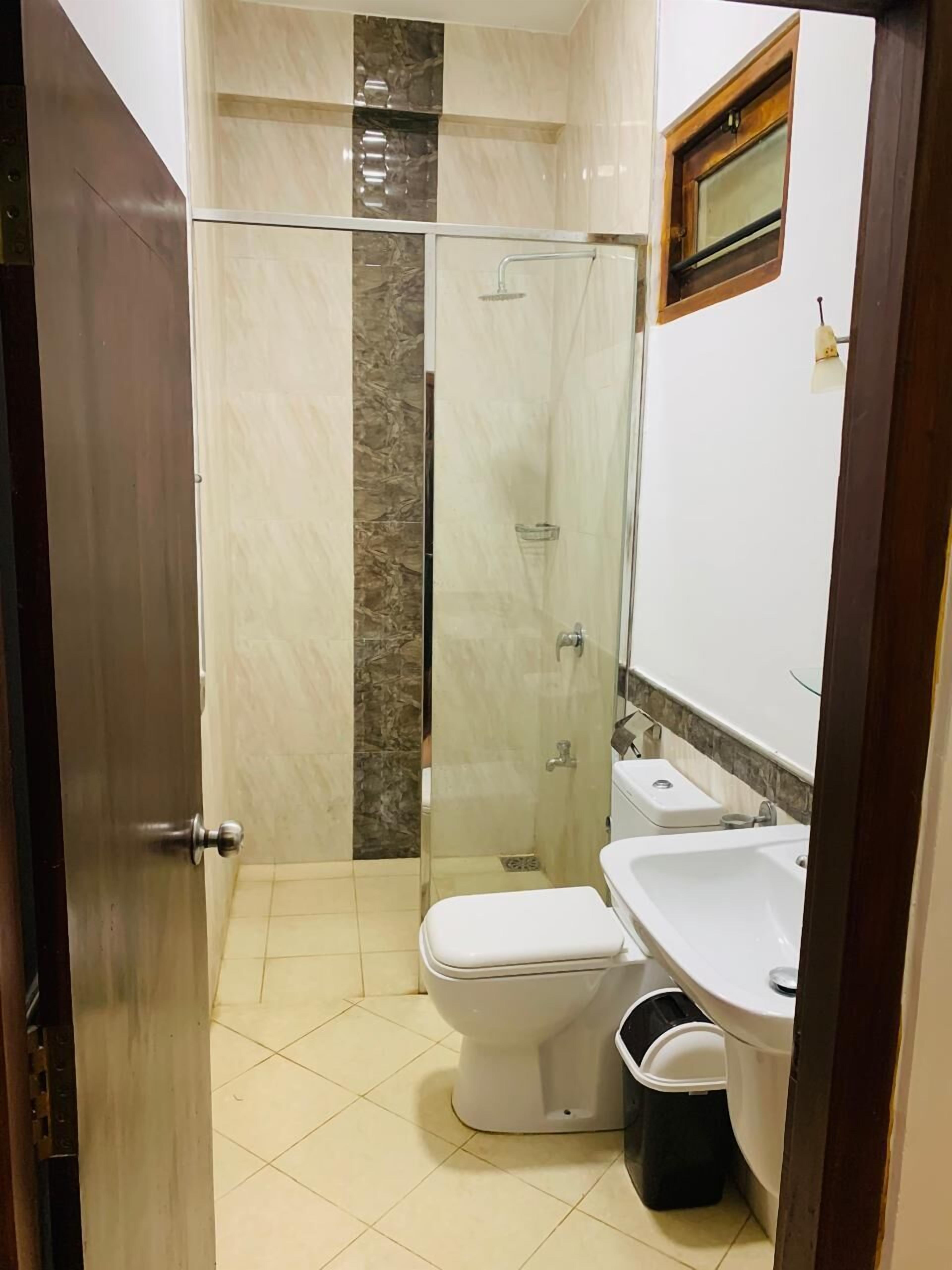 A bathroom with a glass-enclosed shower, a toilet, a sink, and a trash bin.