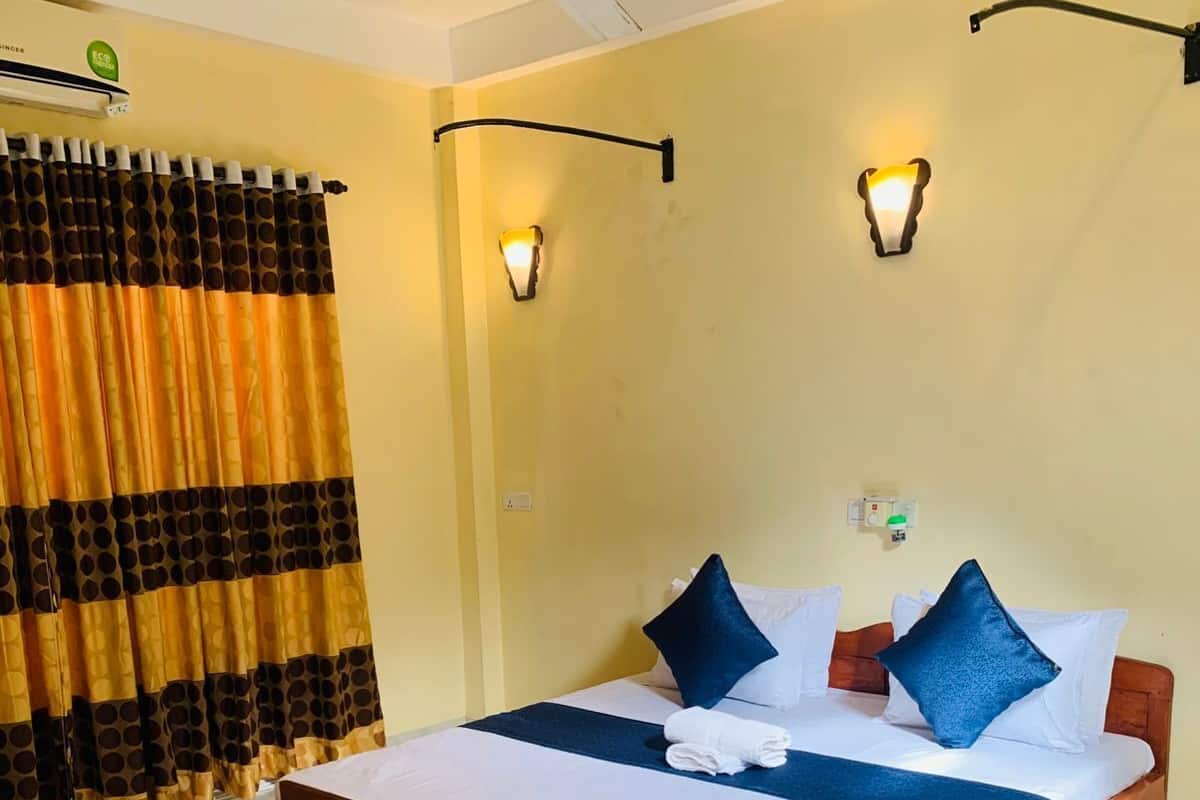Une chambre d’hôtel avec un lit, des rideaux, un ventilateur de plafond, des lampes fixées au mur et un sol carrelé.