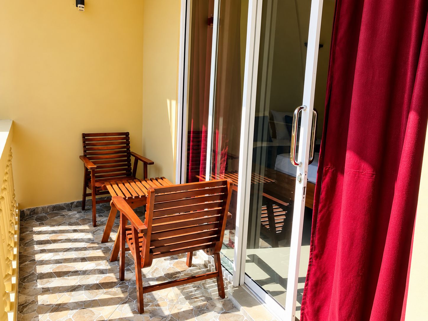A balcony with wooden furniture and a glass door leading to a room.