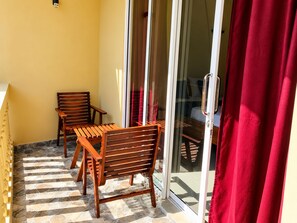 A balcony with wooden furniture and a glass door leading to a room. - Deergayu Homestay  (Mirissa)