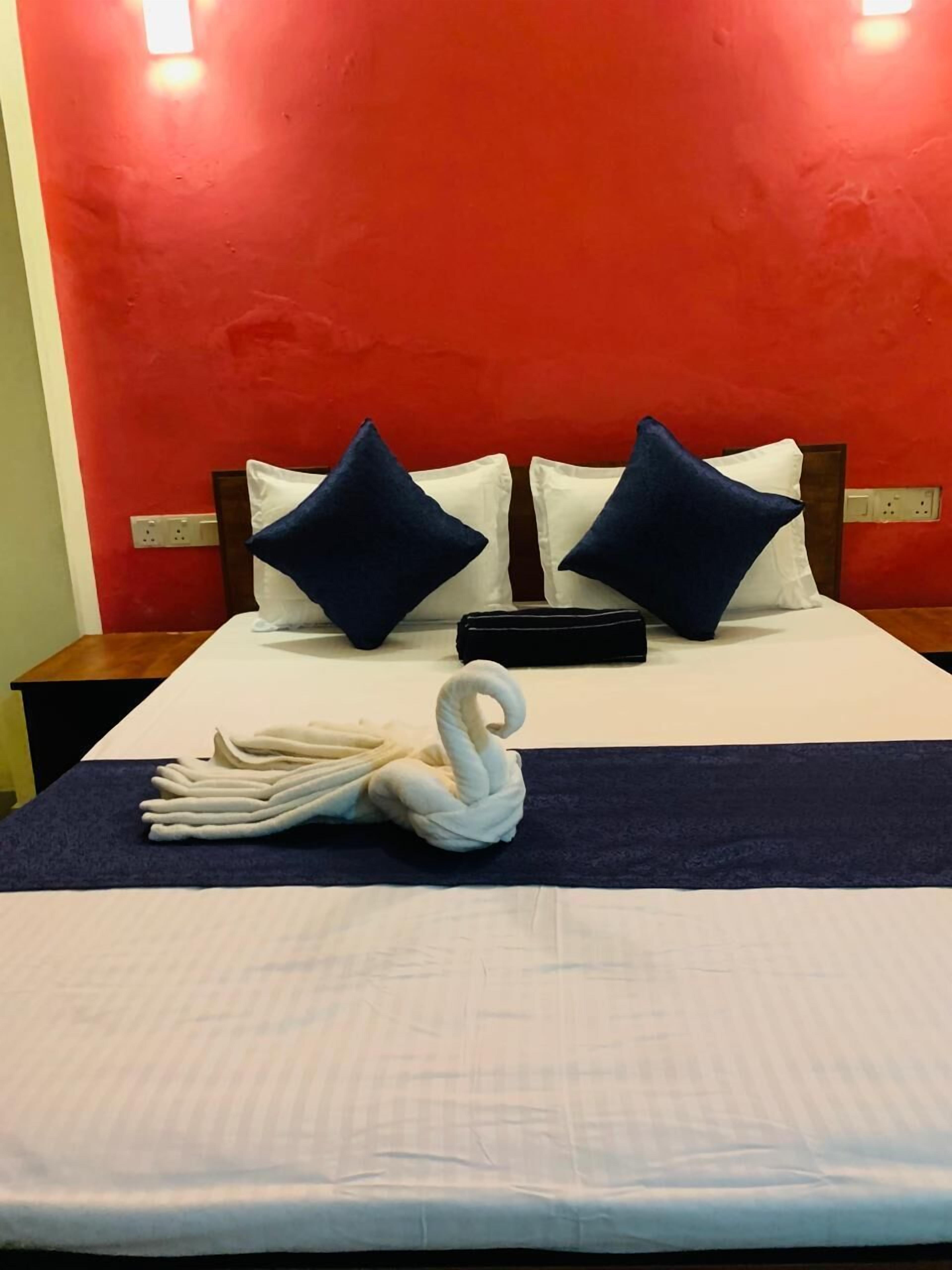 Une chambre d’hôtel avec un mur d’accent rouge, un lit soigneusement fait avec une literie blanche et bleue, et une serviette en forme de cygne décorative posée sur le lit.