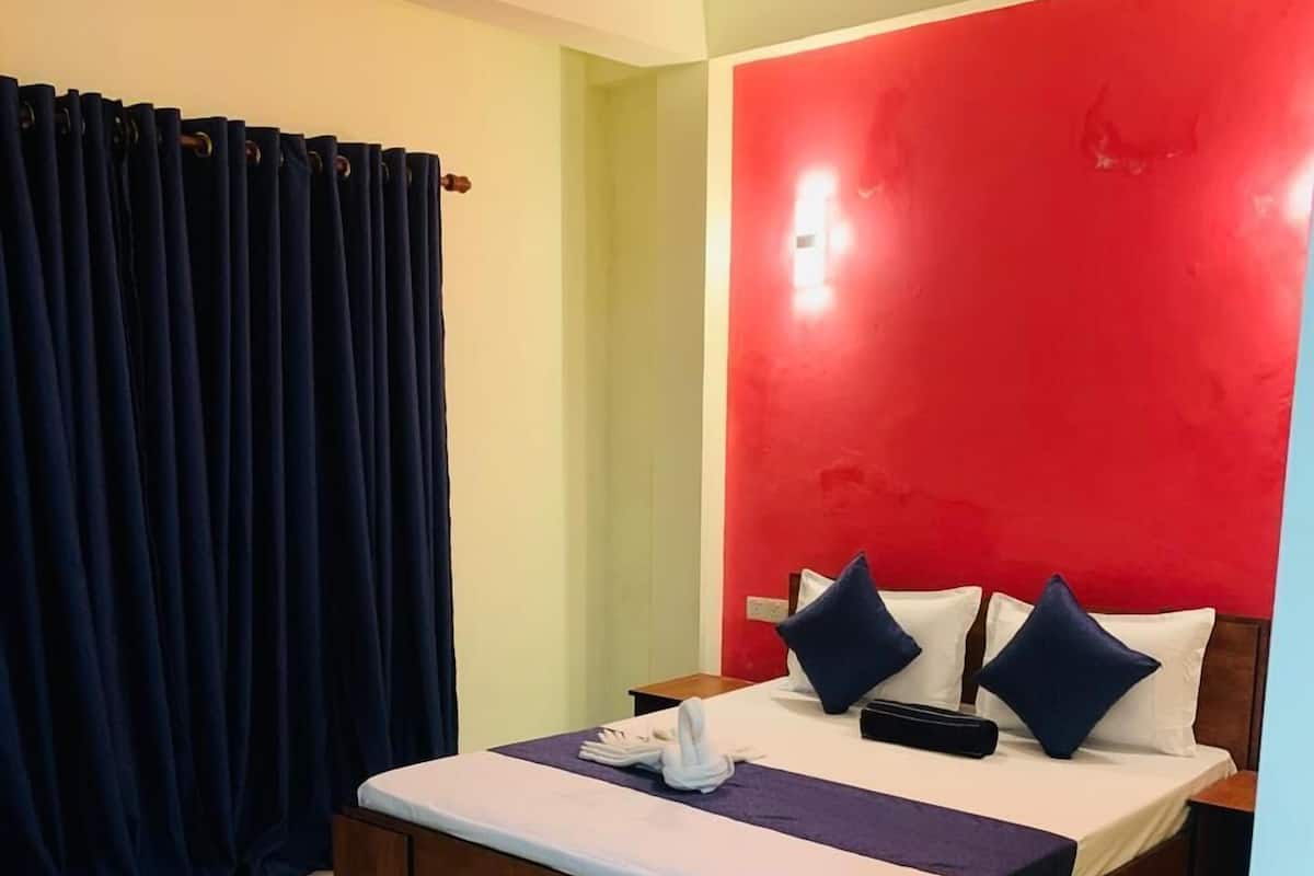 Une chambre d’hôtel avec un lit, une table de chevet en bois, un ventilateur de plafond et un mur d’accent rouge.