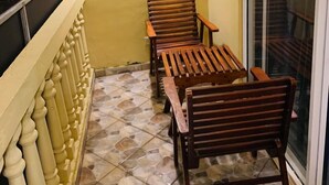A balcony with two wooden chairs and a small table, a light fixture on the wall, and a sliding glass door. - Deergayu Homestay  (Mirissa)