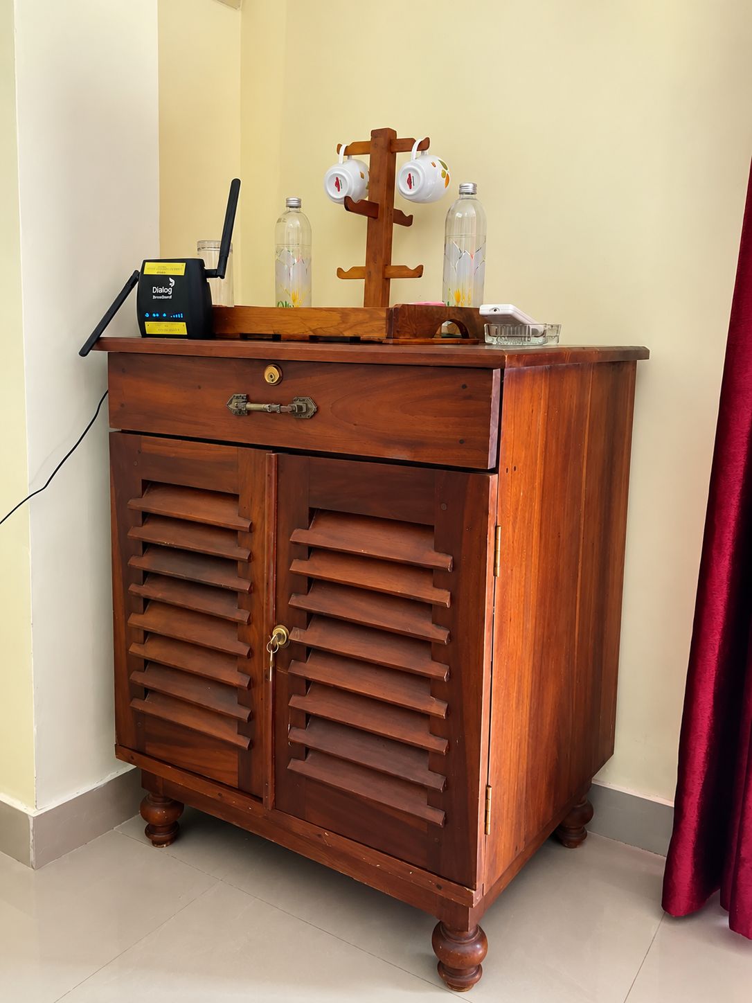 A wooden cabinet with two drawers and a shelf, containing a router, a router box, and two glass bottles.